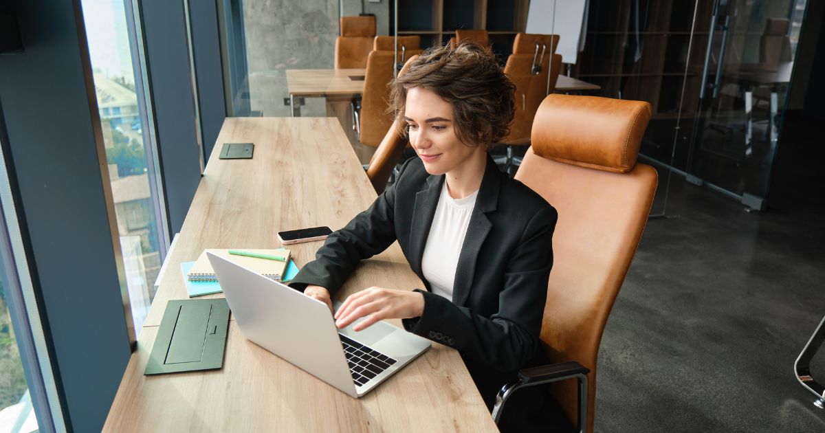 An executive assistant in a black suit working at a laptop in a cowork space