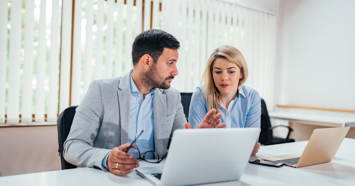 Two company founders sitting at a meeting table comparing calendars on their laptops