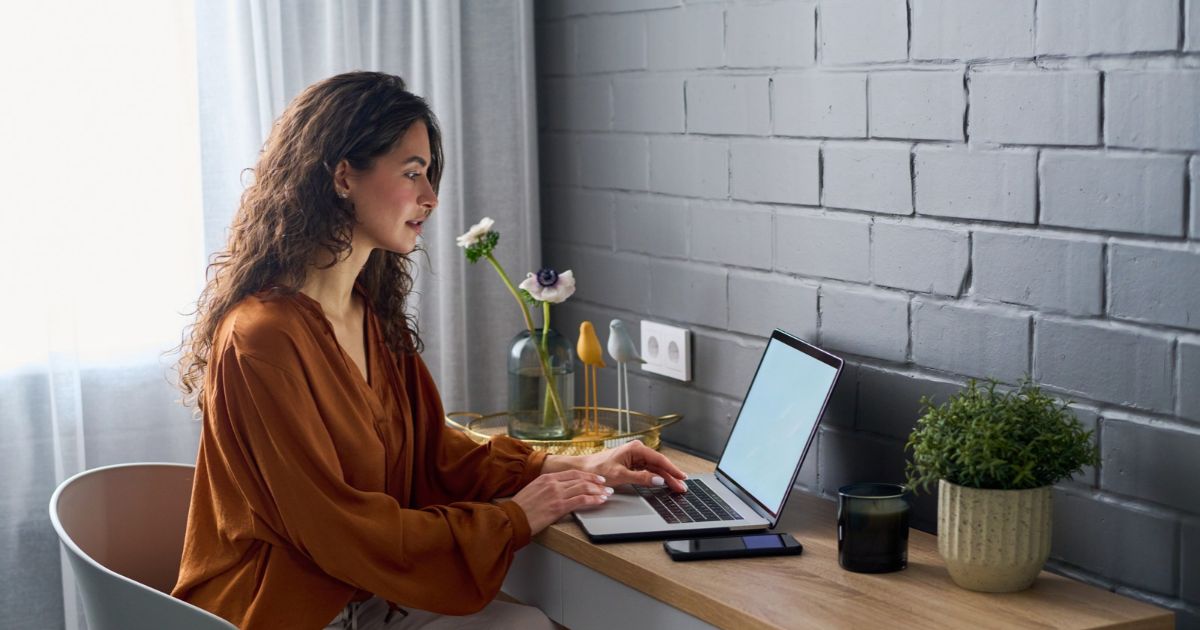 An executive assistant at a home office desk working through two founders’ calendars on a laptop