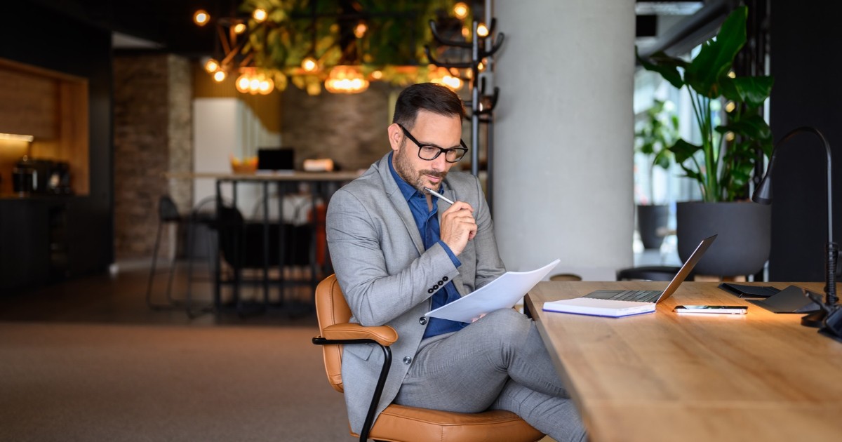 A founder at a wooden desk reading a printed contract with a pen in hand