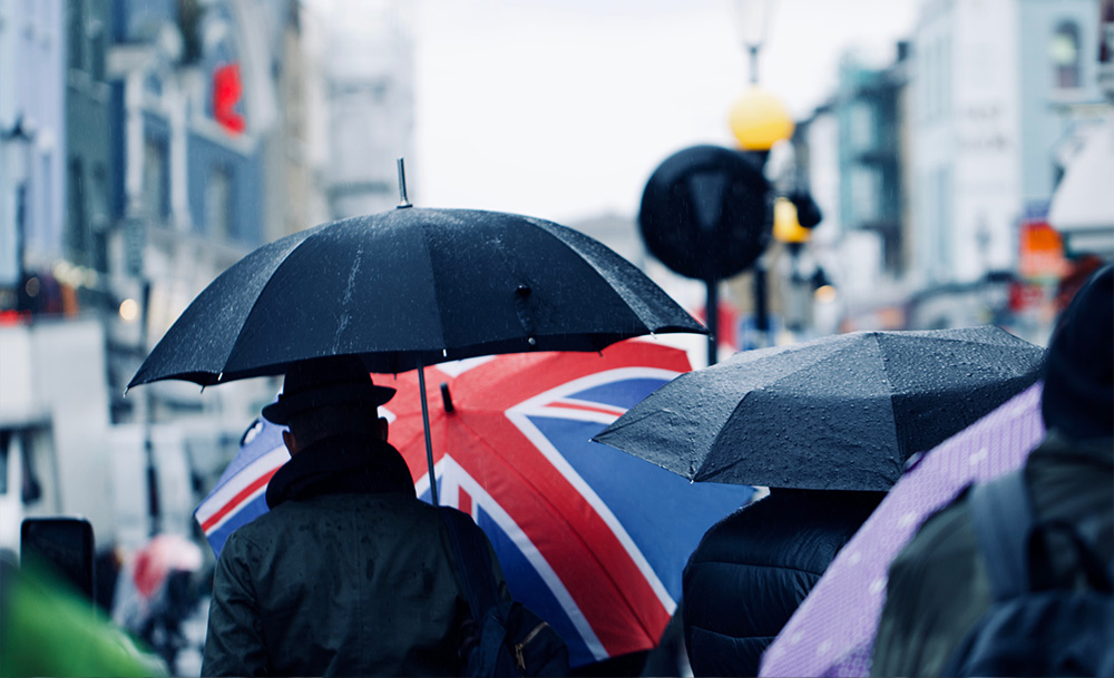 A CEO in London stands out from a crowd with a colored umbrella, a visual metaphor for the business agility and flexibility gained when you outsource your executive assistant.