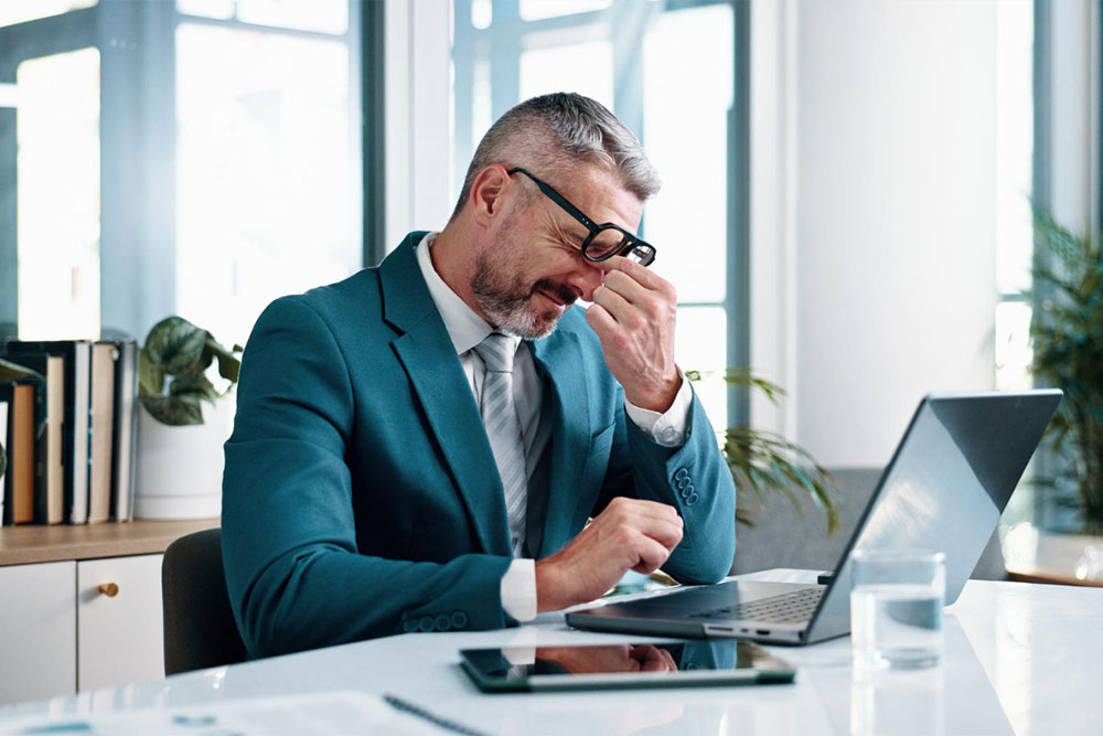 A stressed business leader reviewing and correcting documents in an office, representing the common mistakes of perfectionism and reverse delegation that hinder effective leadership.