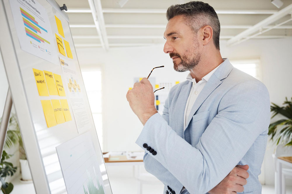 A business leader sketching a progression of steps on a whiteboard, illustrating the "Delegation Ladder" concept from simple task execution to full strategic ownership.