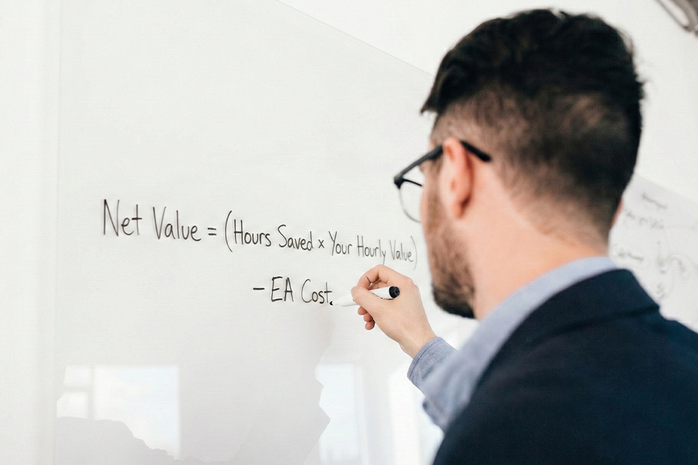 A business professional calculating the return on investment (ROI) of an executive assistant using a financial formula on a glass board.