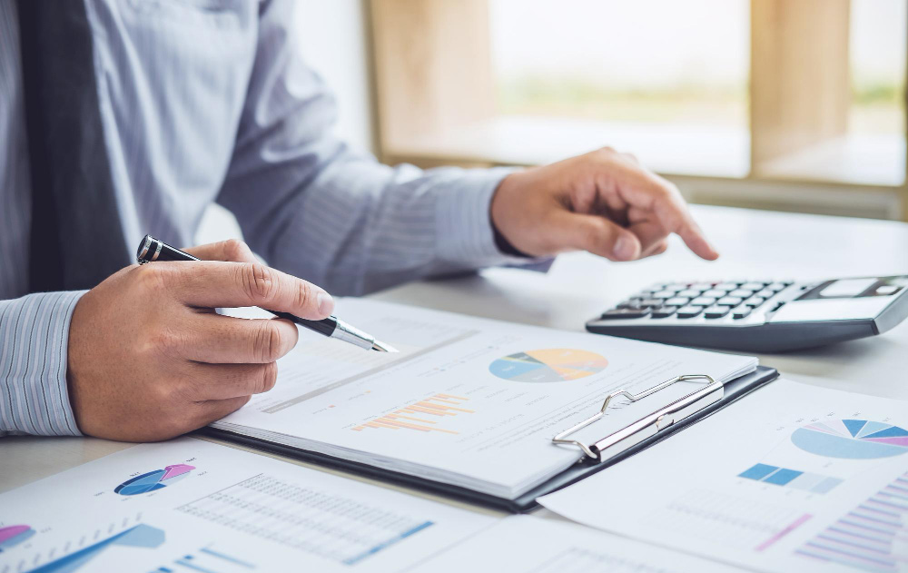 Close-up of a business professional using a calculator and reviewing financial charts on a tablet, calculating the total cost of hiring a full-time executive assistant.