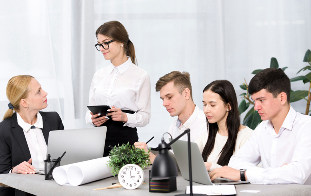 Five professional candidates sitting in a corporate waiting area, reviewing documents and preparing for an executive assistant job interview.